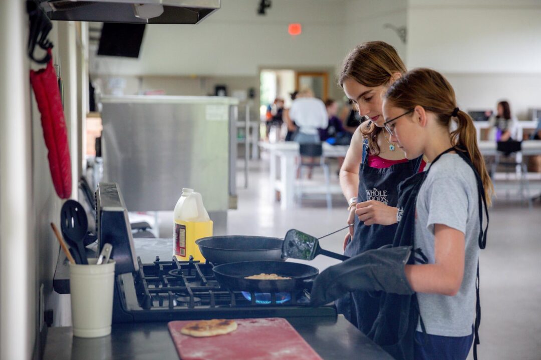 two girls cooking over a stovetop